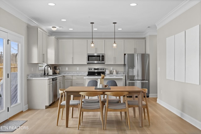 kitchen featuring crown molding, light countertops, light wood-style flooring, appliances with stainless steel finishes, and a sink