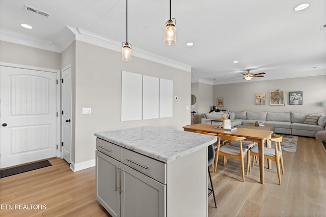 kitchen with a center island, pendant lighting, visible vents, light wood-style flooring, and ornamental molding