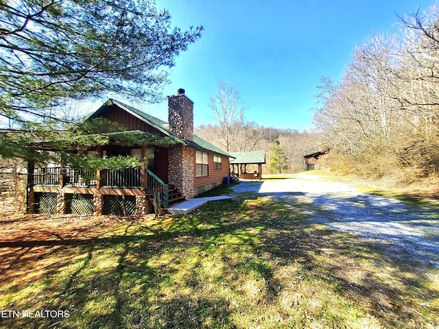 view of side of property with driveway, a chimney, and a yard