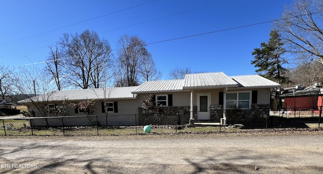 view of front of property featuring stone siding, a fenced front yard, and metal roof