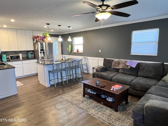 living area featuring recessed lighting, a wainscoted wall, wood finished floors, a ceiling fan, and crown molding