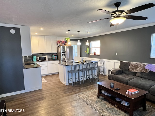 living area featuring a ceiling fan, ornamental molding, wainscoting, a textured ceiling, and wood finished floors