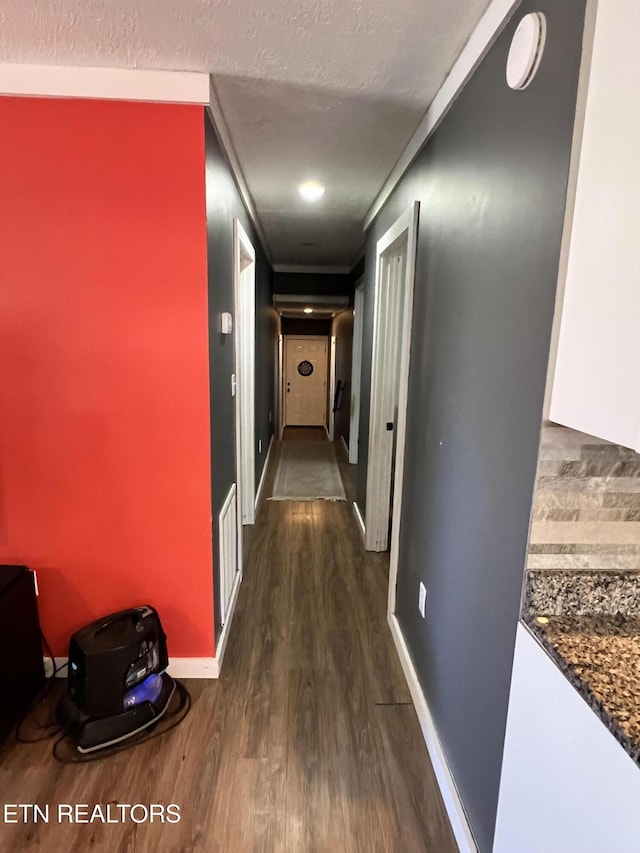 hall featuring dark wood-style flooring, visible vents, a textured ceiling, and baseboards