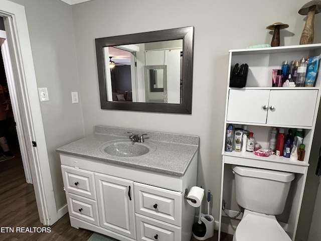 bathroom with toilet, wood finished floors, vanity, and baseboards