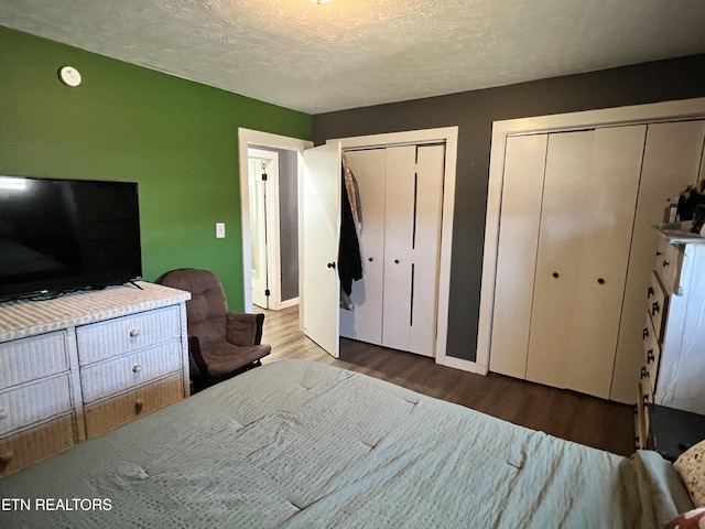 bedroom featuring a textured ceiling, two closets, and wood finished floors