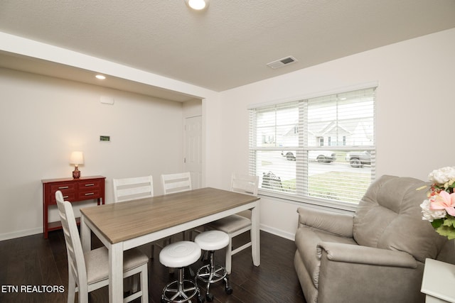 dining space featuring visible vents, dark wood finished floors, a textured ceiling, and baseboards