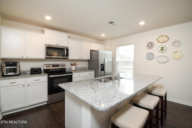 kitchen featuring stainless steel appliances, a sink, visible vents, white cabinets, and a kitchen breakfast bar