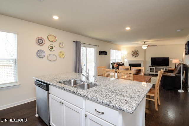 kitchen featuring dark wood-type flooring, stainless steel dishwasher, a fireplace, white cabinetry, and a sink