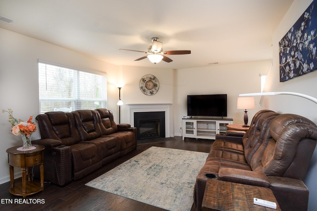 living room featuring dark wood-type flooring, visible vents, a fireplace with flush hearth, and a ceiling fan