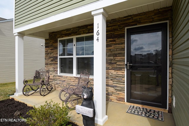 view of exterior entry with stone siding and covered porch