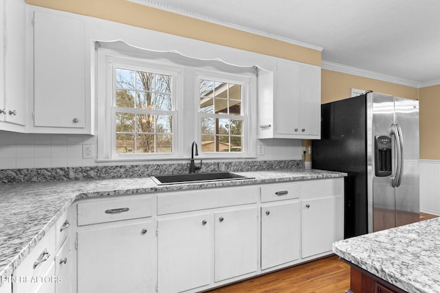 kitchen featuring a sink, white cabinetry, light countertops, stainless steel fridge, and crown molding