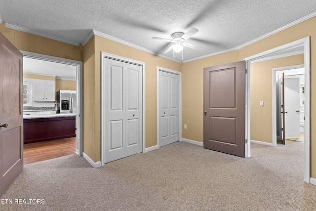 unfurnished bedroom featuring ornamental molding, stainless steel refrigerator with ice dispenser, carpet flooring, and multiple closets