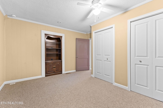 unfurnished bedroom featuring multiple closets, crown molding, a textured ceiling, and carpet flooring