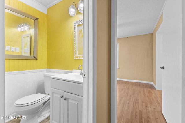 bathroom with a textured ceiling, toilet, wood finished floors, vanity, and ornamental molding