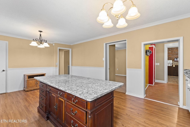 kitchen featuring light wood-type flooring, wainscoting, a notable chandelier, and decorative light fixtures