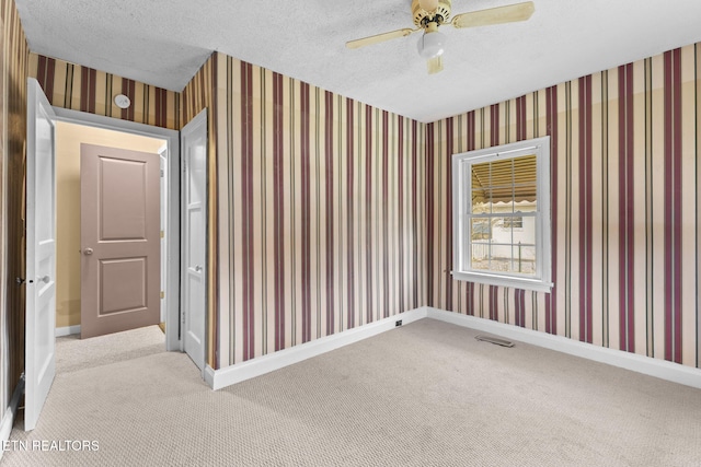 carpeted empty room with a textured ceiling, baseboards, and wallpapered walls