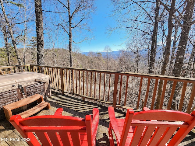 wooden terrace with a hot tub and a view of trees