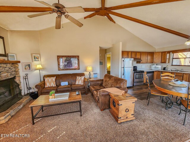 living area with a ceiling fan, beamed ceiling, a stone fireplace, and high vaulted ceiling