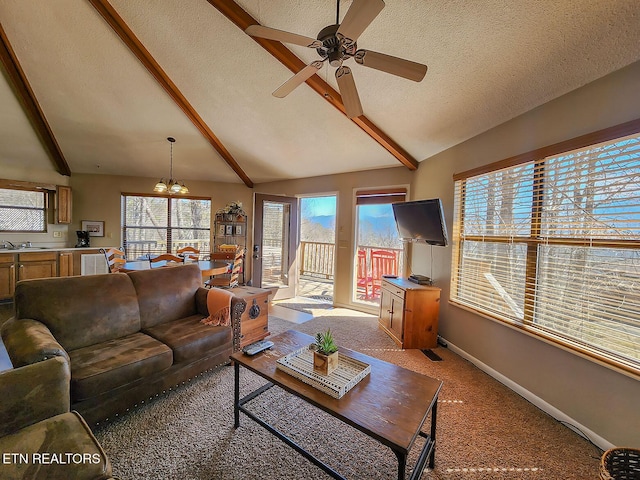 living area with lofted ceiling with beams, a textured ceiling, light colored carpet, ceiling fan with notable chandelier, and baseboards