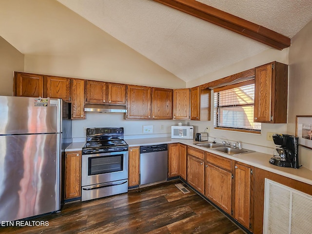 kitchen with brown cabinetry, lofted ceiling with beams, stainless steel appliances, under cabinet range hood, and a sink