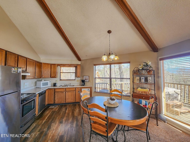 kitchen with vaulted ceiling with beams, under cabinet range hood, stainless steel appliances, a sink, and brown cabinetry