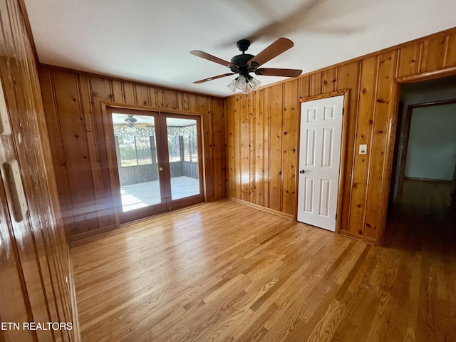 empty room with wooden walls, baseboards, light wood-style flooring, ceiling fan, and french doors