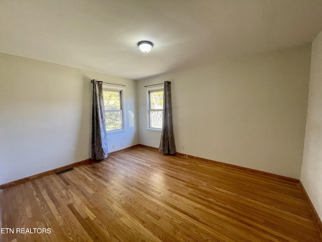 spare room with light wood finished floors, visible vents, and baseboards