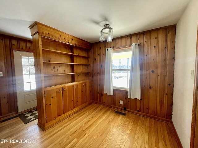 unfurnished dining area with light wood finished floors, plenty of natural light, and wood walls