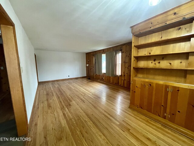 unfurnished living room featuring light wood-style floors, baseboards, and wood walls