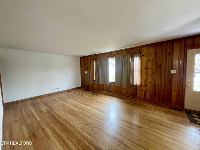 unfurnished living room with visible vents, light wood-style flooring, wood walls, and baseboards