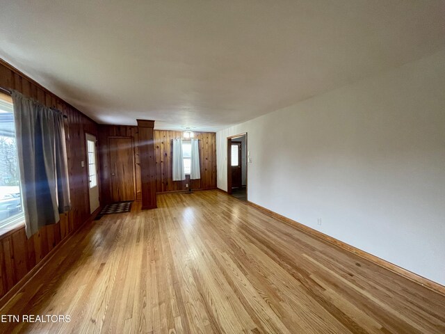 unfurnished living room featuring baseboards, wood walls, and light wood finished floors