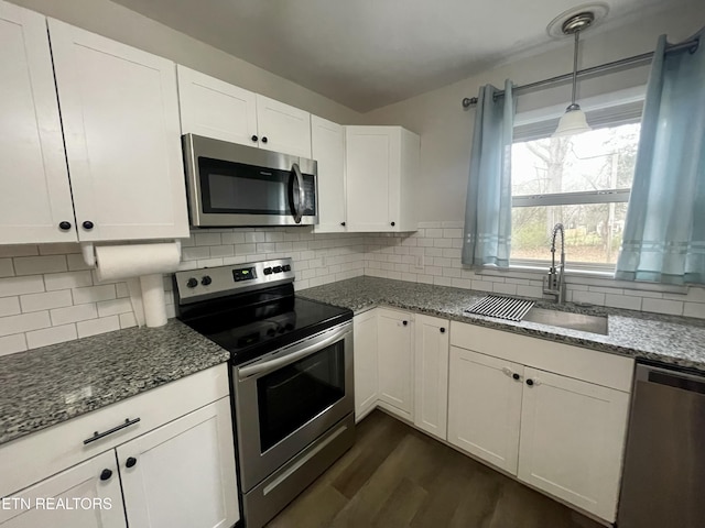 kitchen with dark stone countertops, a sink, decorative backsplash, dark wood-type flooring, and stainless steel appliances