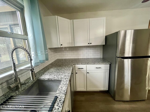 kitchen with backsplash, white cabinets, freestanding refrigerator, and a sink