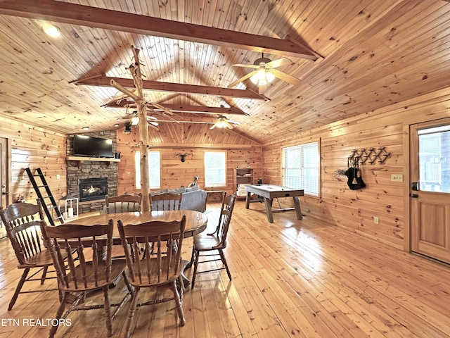 dining space with a ceiling fan, wood walls, lofted ceiling with beams, and hardwood / wood-style floors