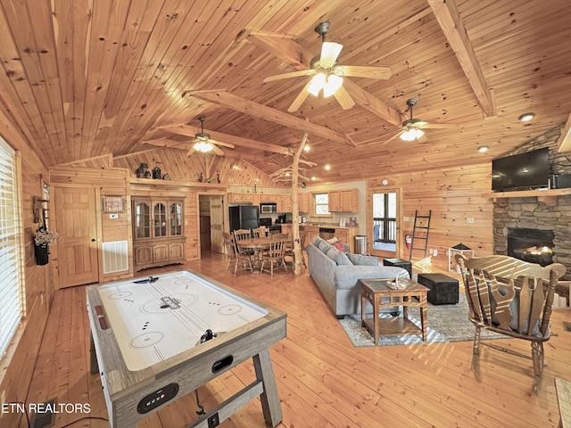 rec room with vaulted ceiling with beams, a stone fireplace, wooden walls, wood ceiling, and light wood-type flooring