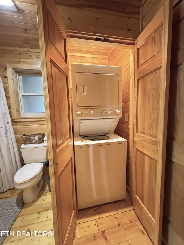 laundry area featuring light wood-style floors, wooden walls, and stacked washer / drying machine