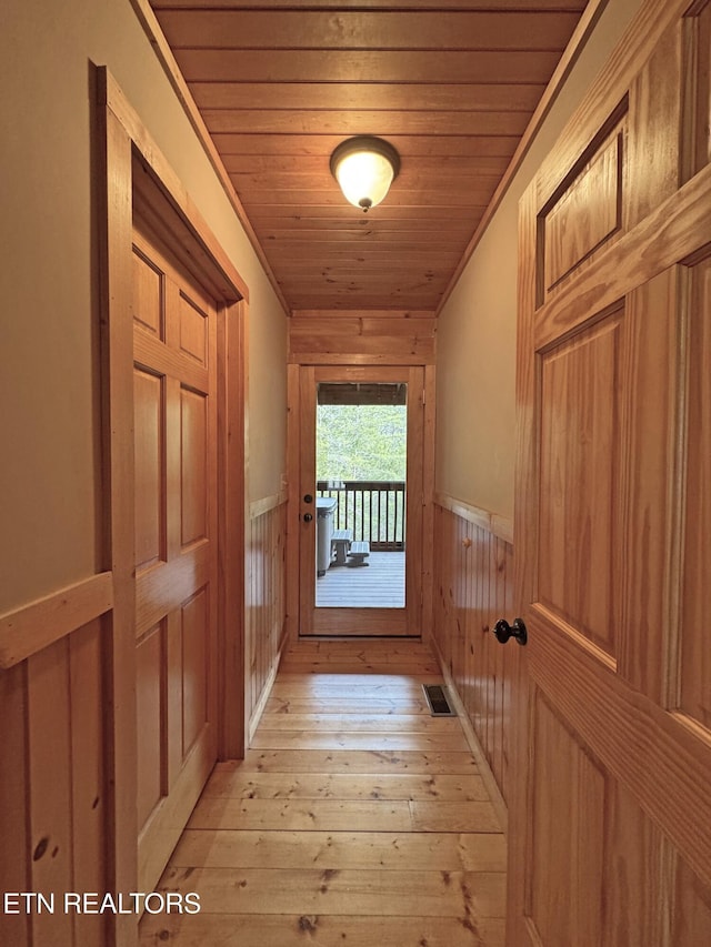 hall featuring visible vents, wainscoting, wooden walls, light wood-type flooring, and wooden ceiling