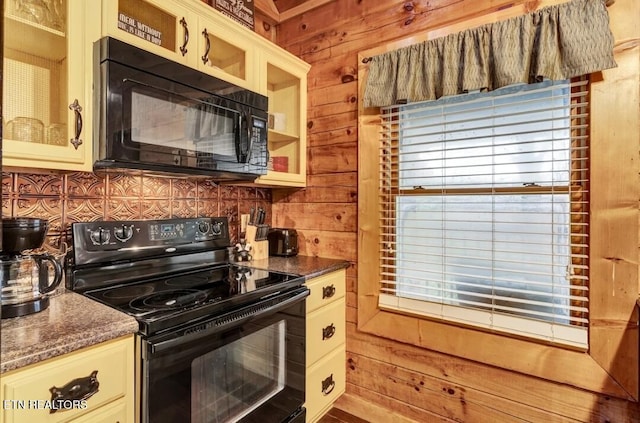 kitchen with black appliances, cream cabinetry, wood walls, and decorative backsplash