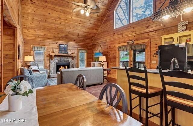 dining area featuring wood walls, a fireplace, wood ceiling, a ceiling fan, and light wood-style floors