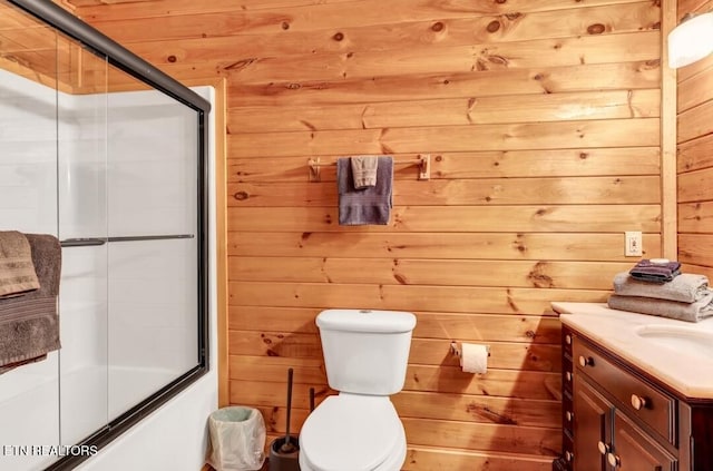 full bath with toilet, bath / shower combo with glass door, wood walls, and vanity