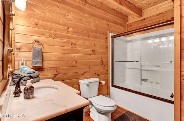 bathroom featuring toilet, combined bath / shower with glass door, wooden walls, vanity, and beamed ceiling