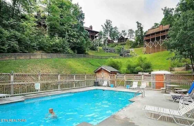 community pool featuring an outbuilding, a patio area, fence, and a lawn