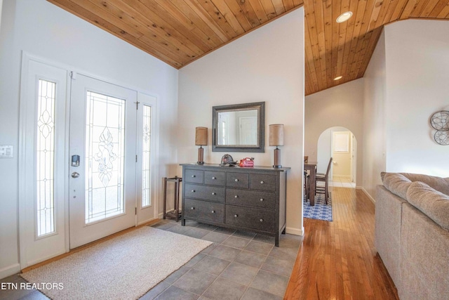 foyer featuring arched walkways, high vaulted ceiling, wooden ceiling, and baseboards