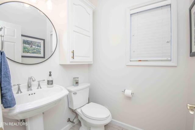 half bathroom with toilet, baseboards, and a sink