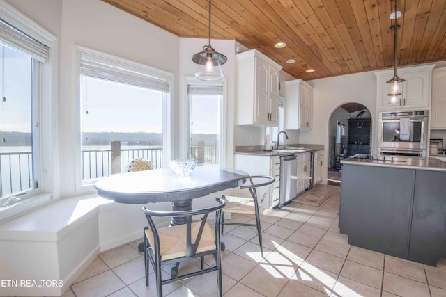 kitchen with stainless steel appliances, arched walkways, white cabinets, and light tile patterned floors