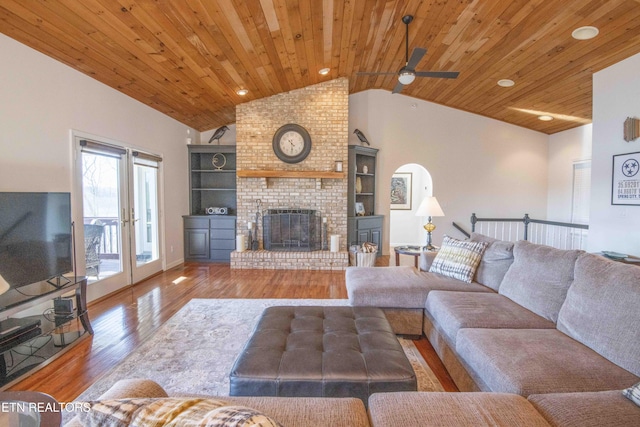 unfurnished living room with arched walkways, lofted ceiling, wood ceiling, a brick fireplace, and wood finished floors