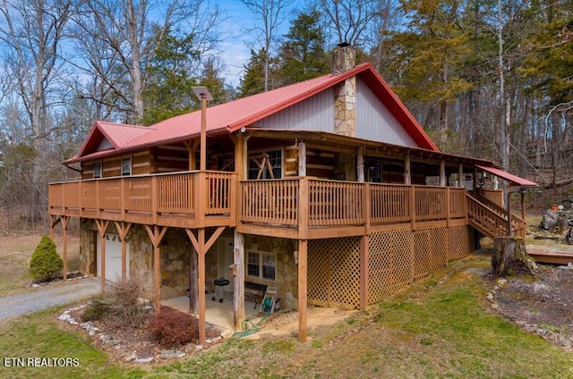 rear view of house with stone siding, a chimney, metal roof, an attached garage, and a deck