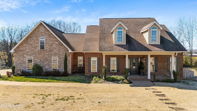 cape cod house with covered porch, a front yard, and brick siding