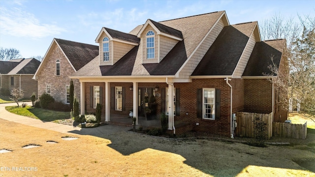 view of front of house with brick siding, a porch, and a shingled roof