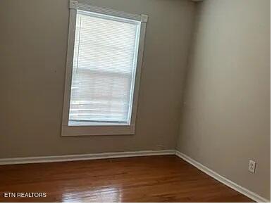 spare room with baseboards and dark wood-type flooring